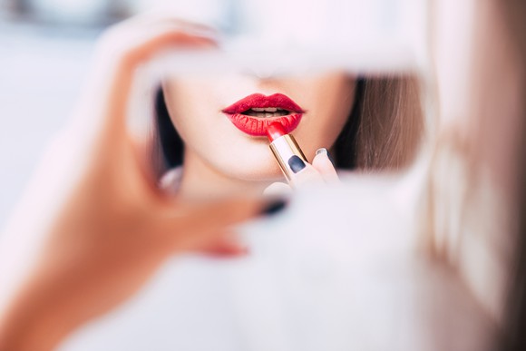 A woman applying lipstick in a handheld mirror.