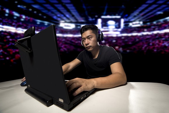 A young man playing a video game on a PC with a large audience in the background