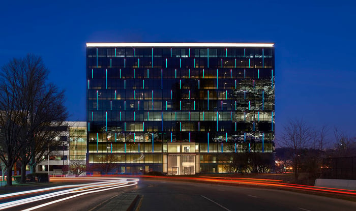 Glass building at dusk with long-exposure streaking headlights.