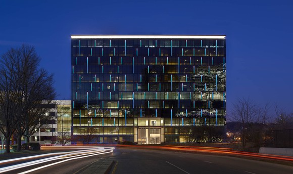 Glass building at dusk with long-exposure streaking headlights.