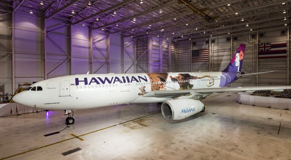 Commercial aircraft with Hawaiian name and logo on it, in a hangar.