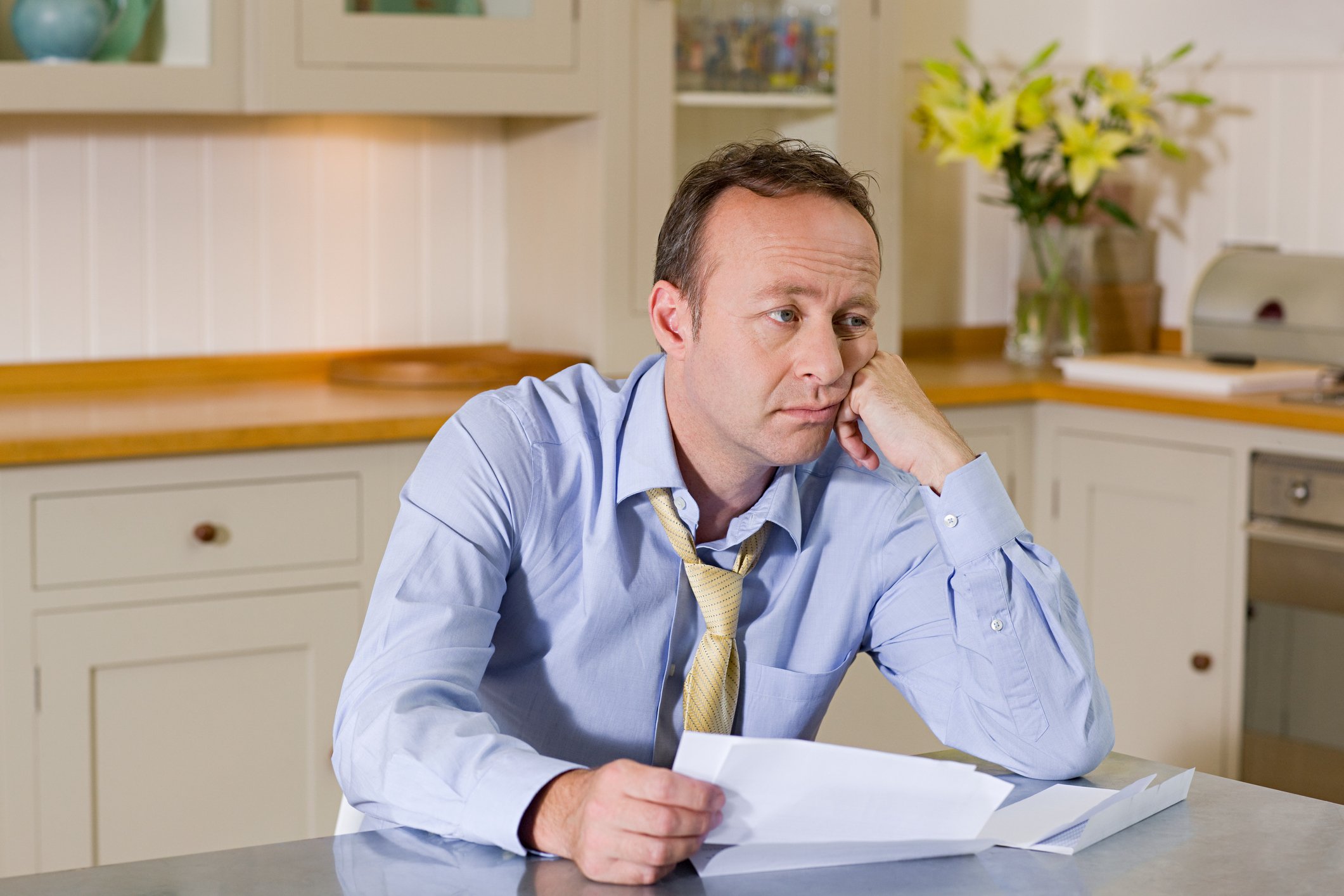 Middle-aged man at table holding documents and looking glum