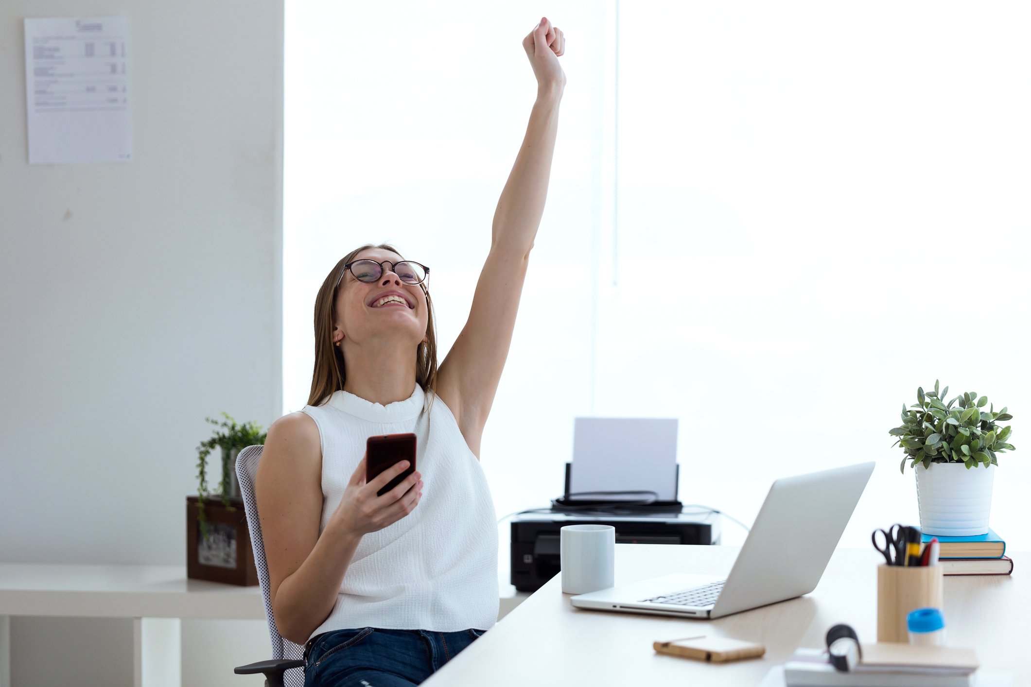Woman at desk holding her arm up as if celebrating