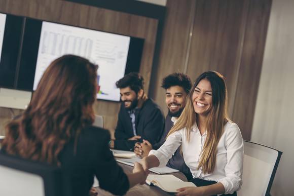 Two women shaking hands in a conference room.