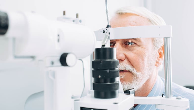 A mature man's eyes being examined by optometrist or ophthalmologist using a phoropter.