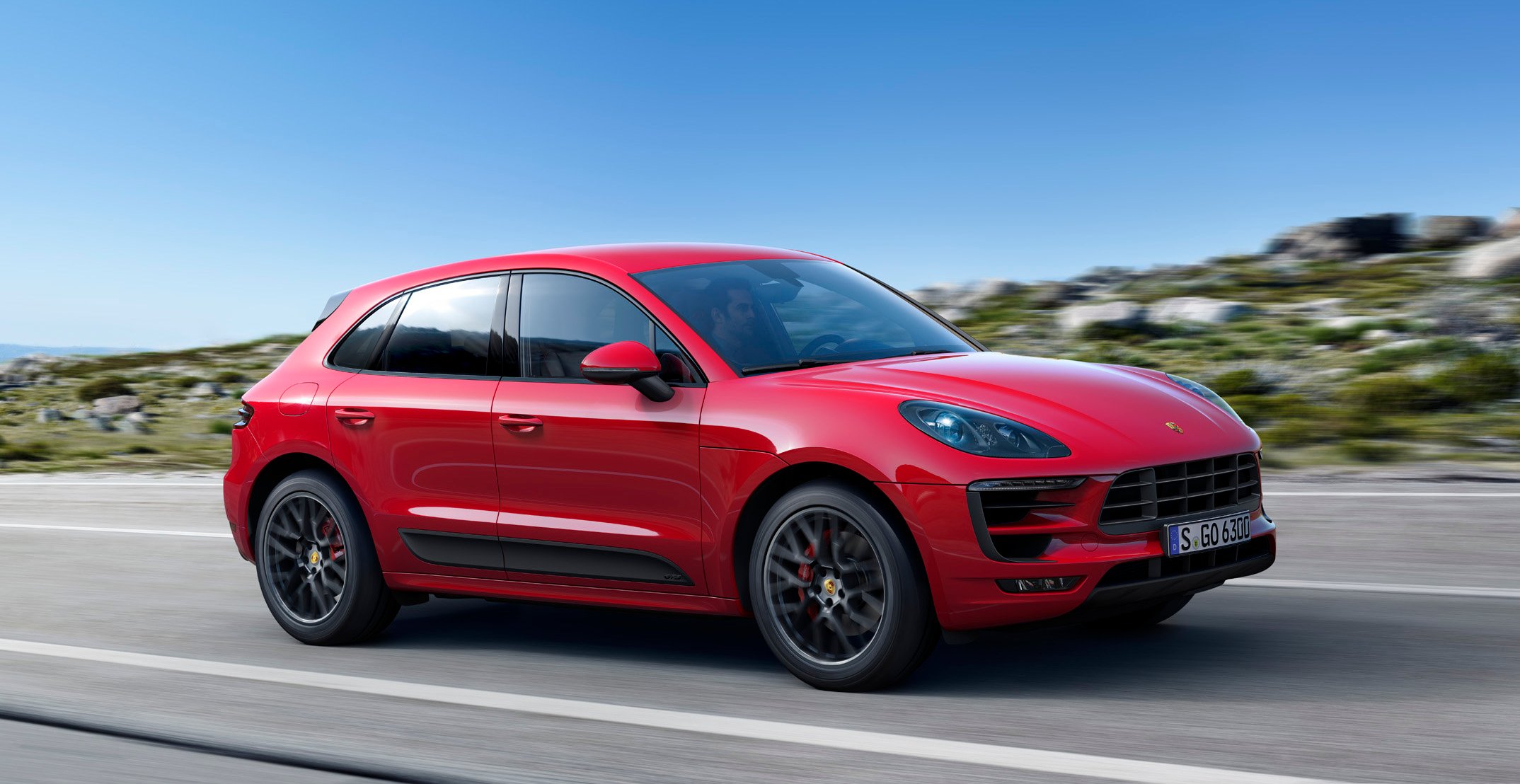 A red Porsche Macan, a sporty compact crossover SUV, on a country road.