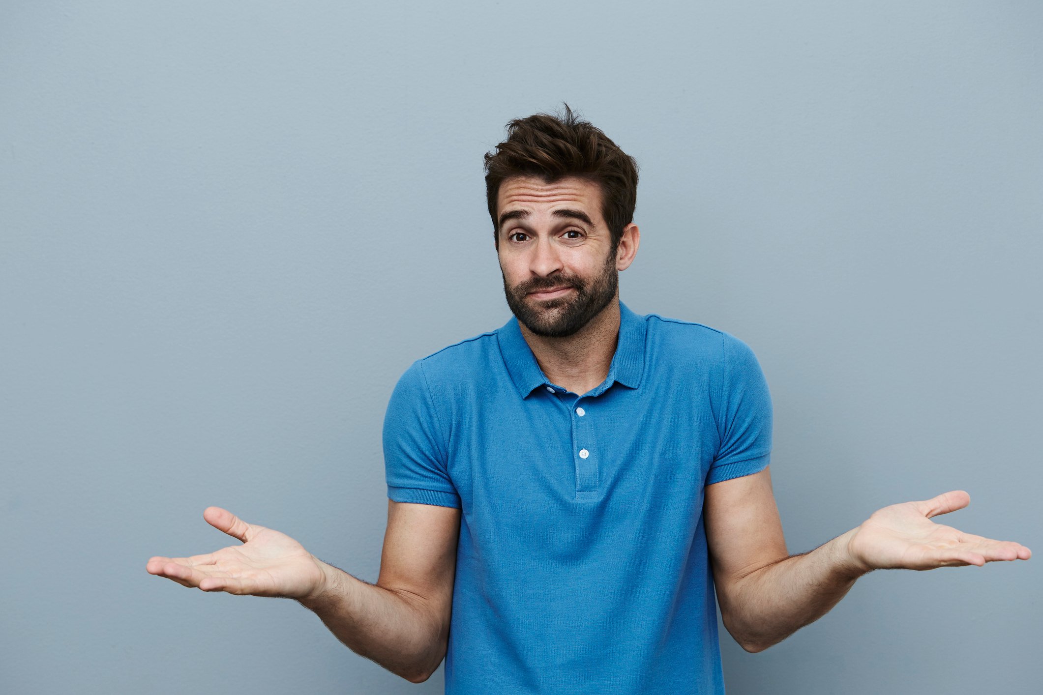 Man in blue polo against gray background shrugging his shoulders