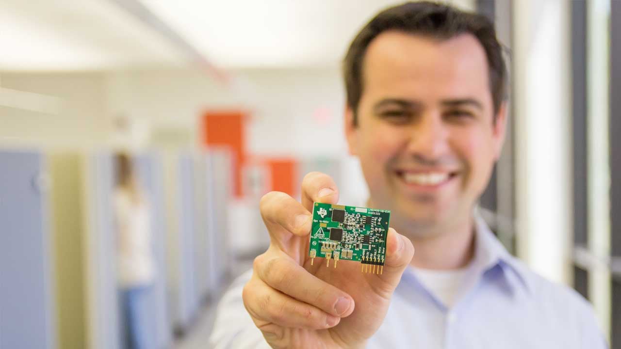 a smiling man holds a microchip in front of him. 
