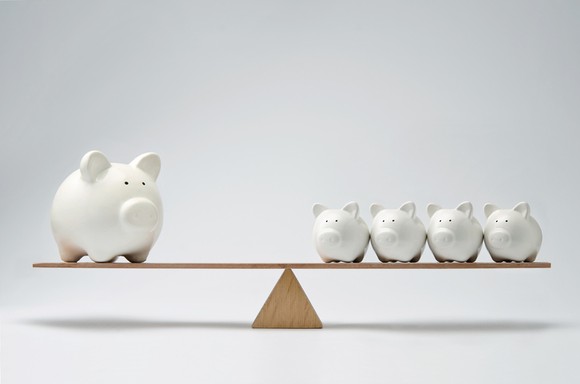 A balanced scale with a giant piggy bank on one end and four smaller piggy banks on the other.