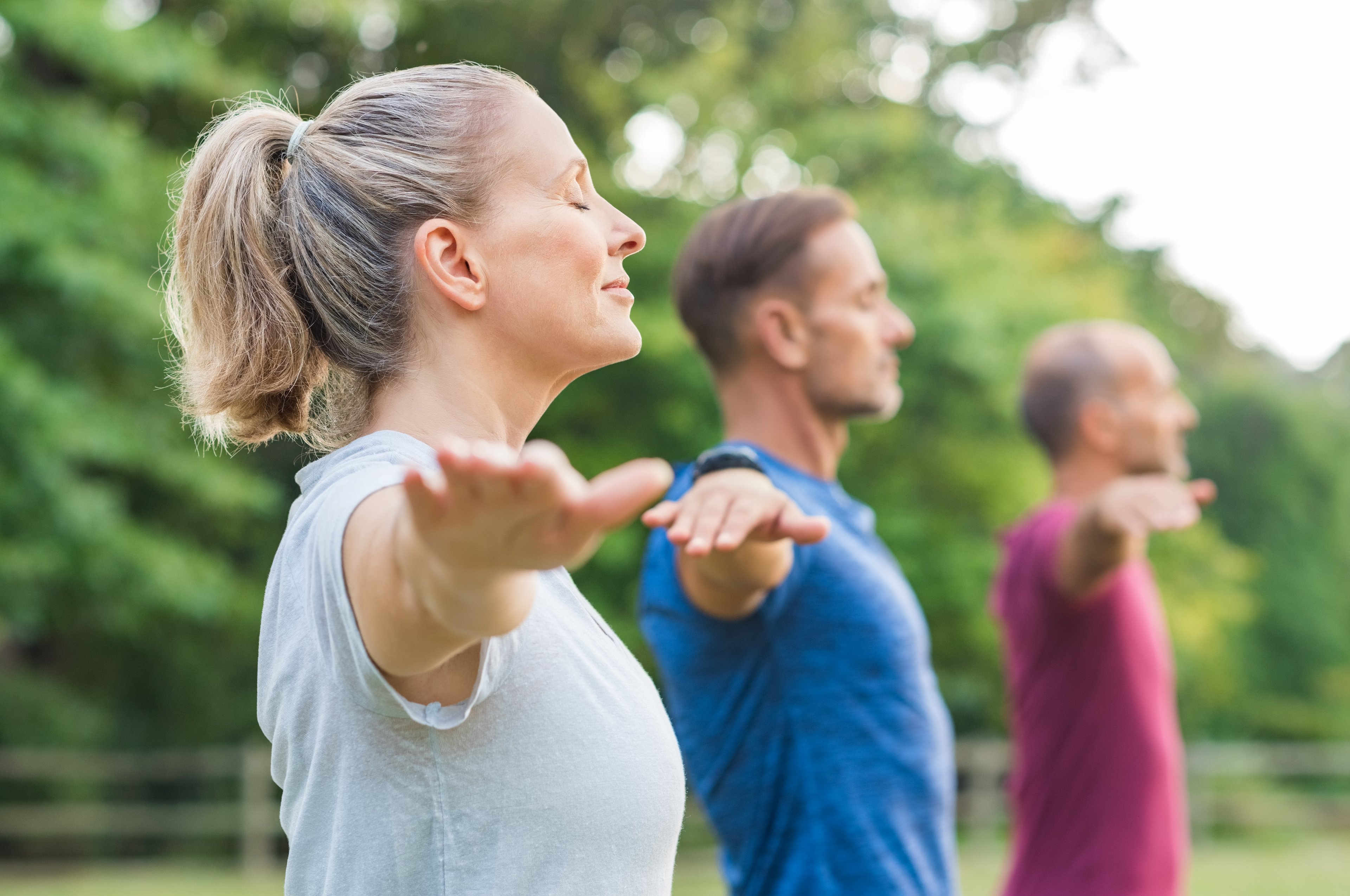A woman and two men close their eyes in a yoga pose