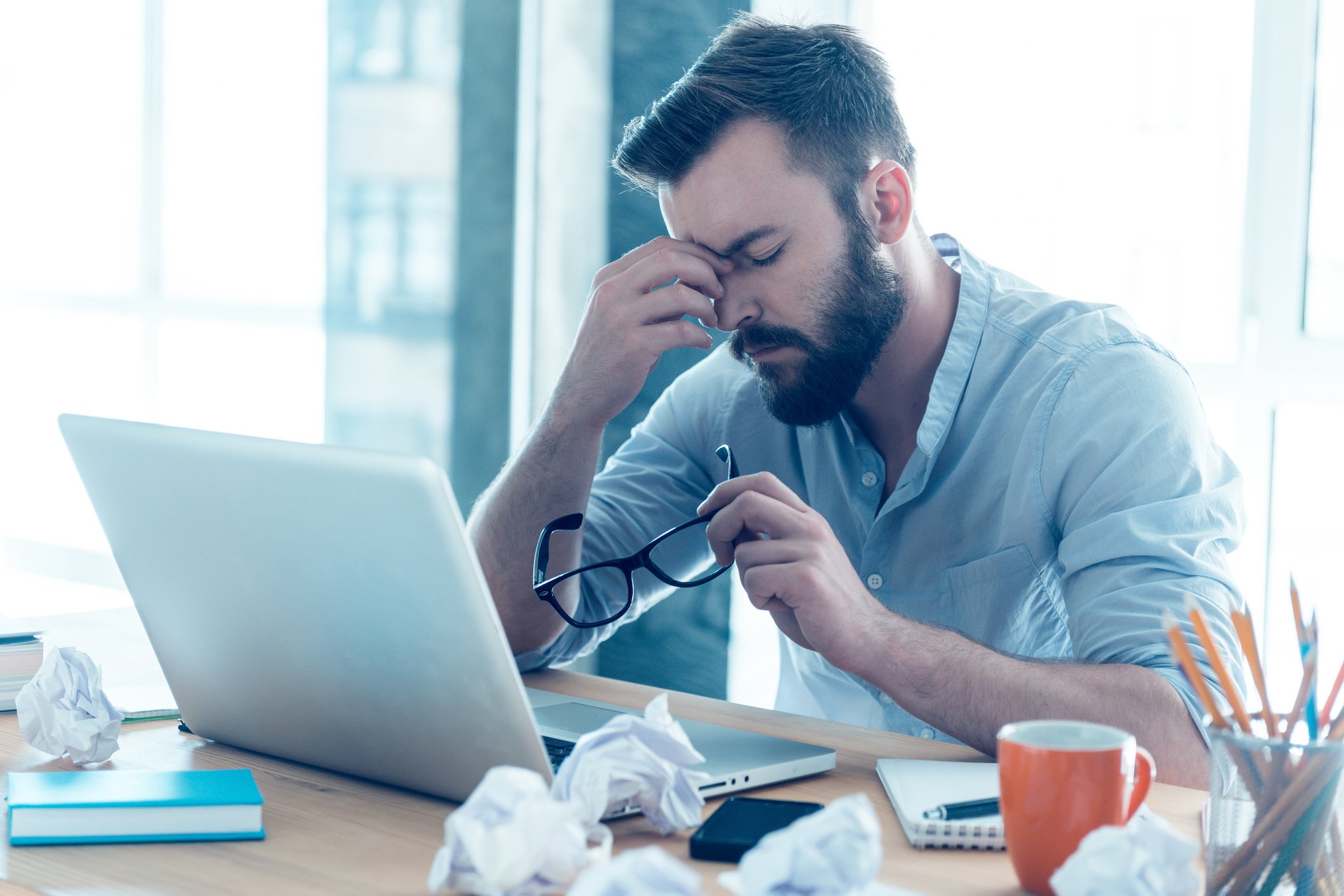 Man at laptop holding his nose and closing his eyes