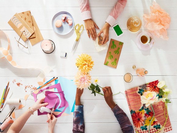 Three pairs of hands working on various arts and crafts at a table.