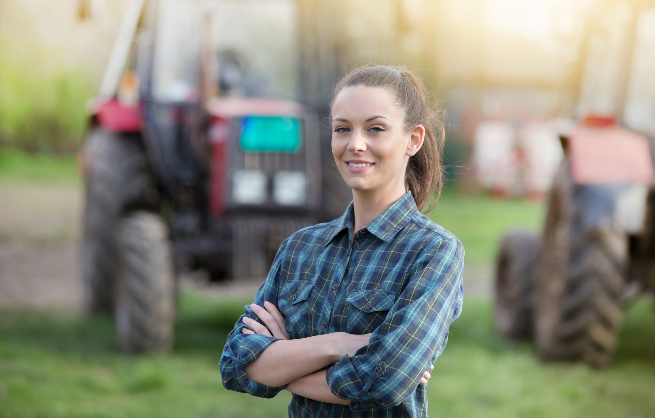 A woman wearing a blue plaid shirt with tractors in the background