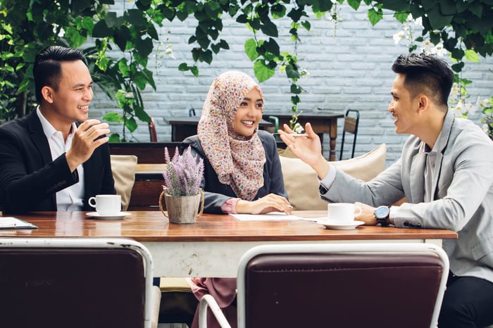 Three people seated around a table and talking.