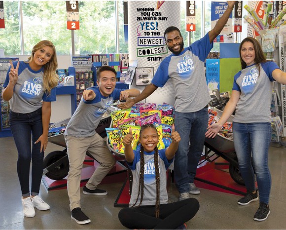 Five Five Below employees smile while posing in company T-shirts in a Five Below store. 