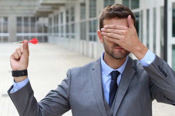 Man in a suit covering his eyes while holding a red dart.