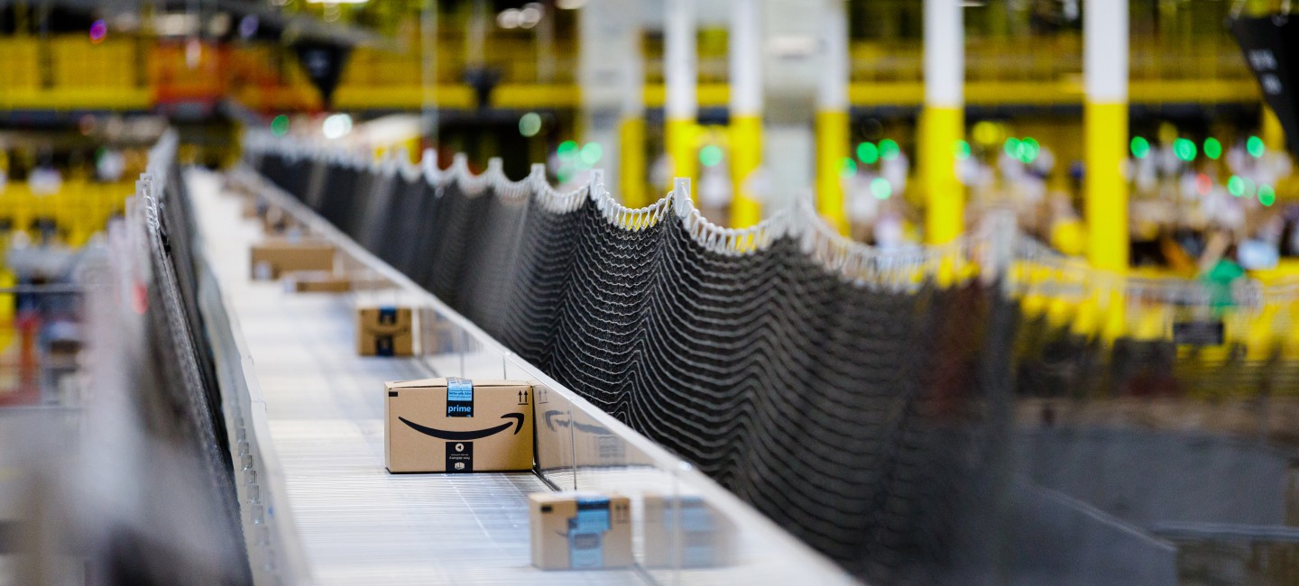 A moving belt of Amazon shipping boxes in a large warehouse facility.