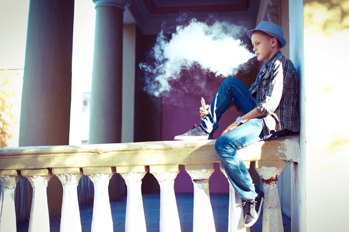 Youth sitting on a railing and vaping.