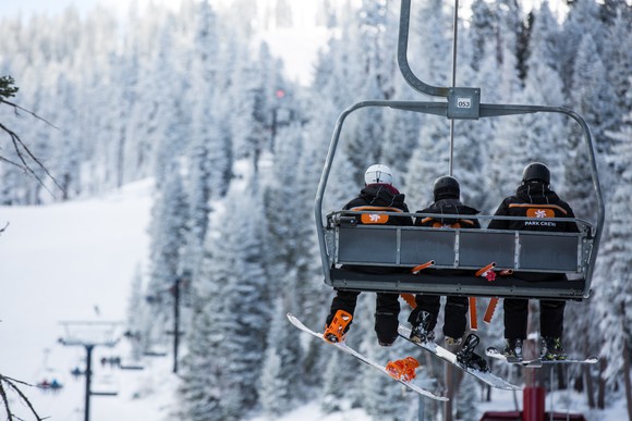 Three skiers riding a chair lift up a snow-covered ski mountain.