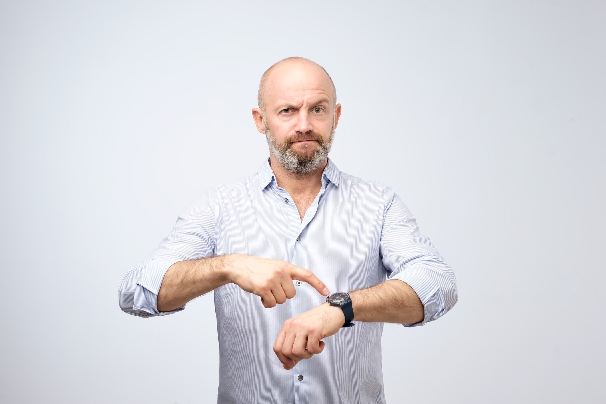 A man with a perturbed expression points to the watch on his wrist.
