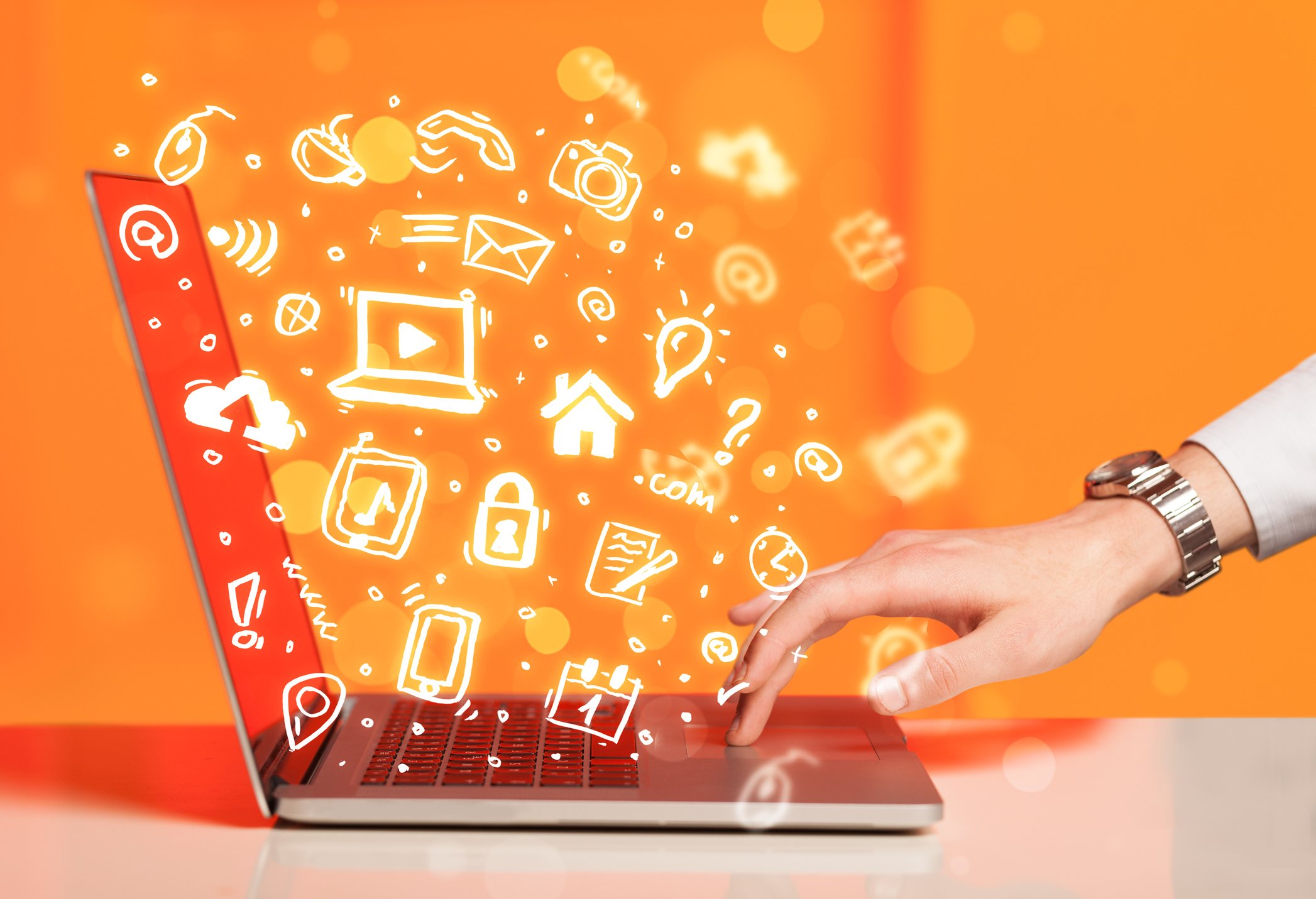 Hand writing on notebook computer with media icons and symbols coming out of it.