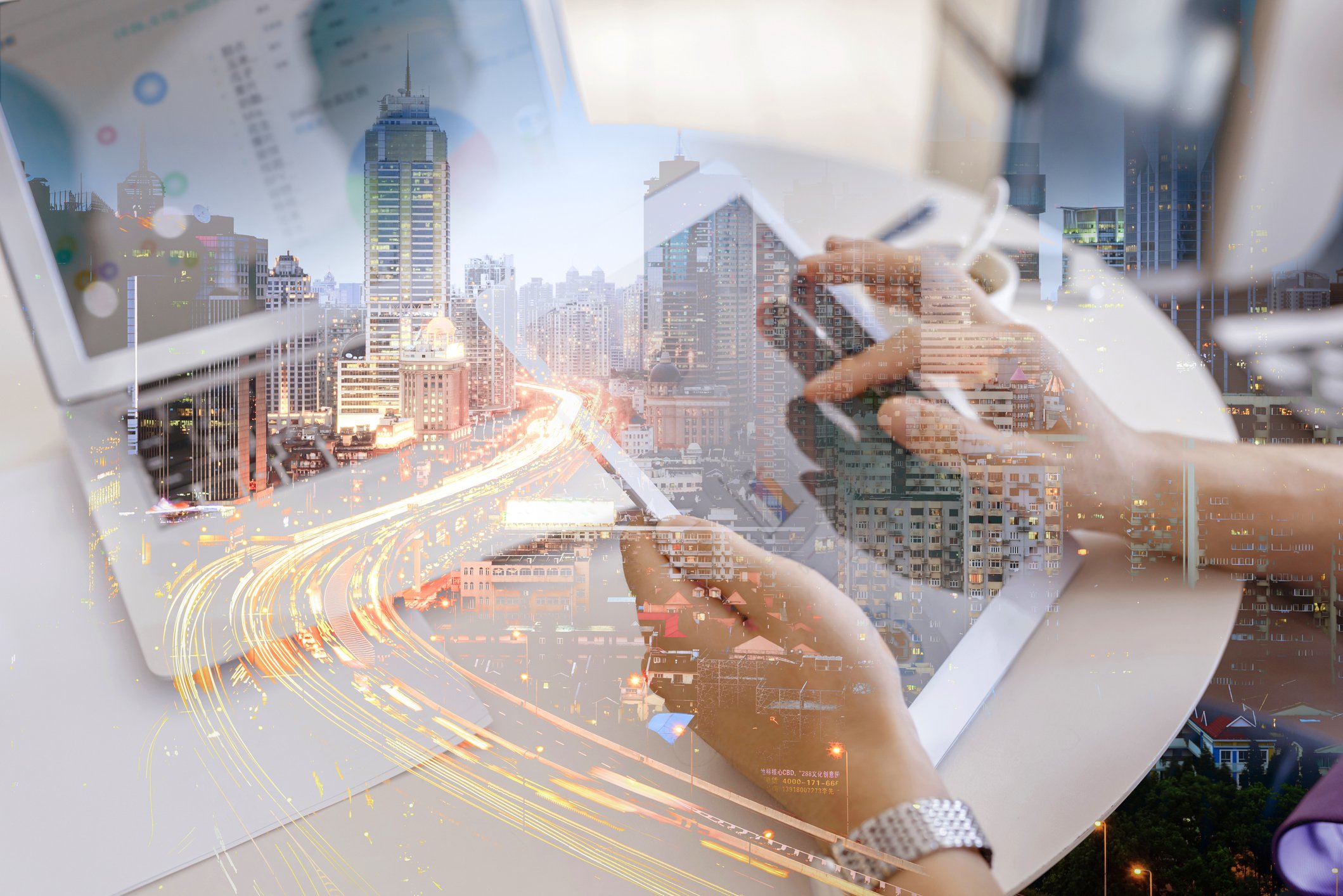 A person working on a tablet, with a second overlaying exposure of cars on a highway in a city