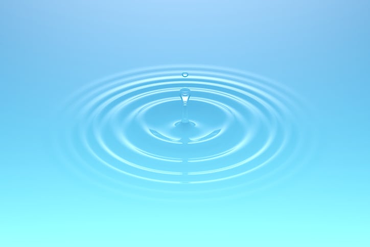 Droplets of water falling into a body of water and creating ripples. Soft light blue-green color.