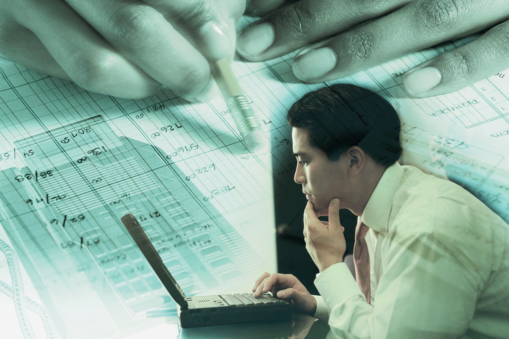 Person going through a ledger hunched over a laptop.