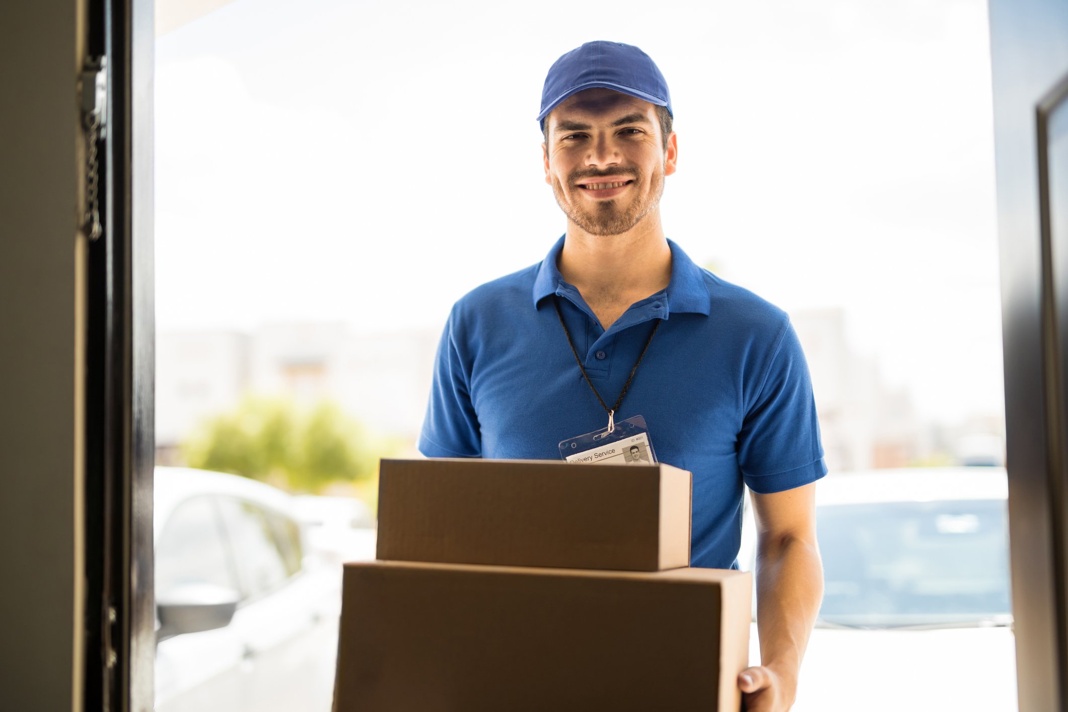 A delivery man smiles and holds packages in a doorway. 