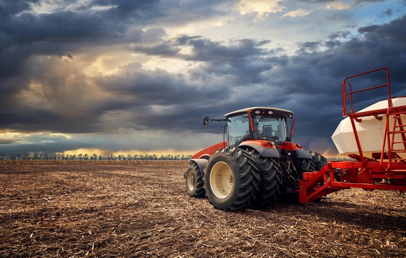 A red tractor in a field with dark clouds overhead.