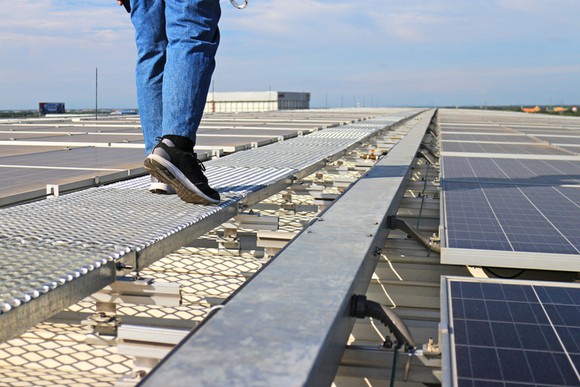 A man walking on a rooftop next to solar panels.