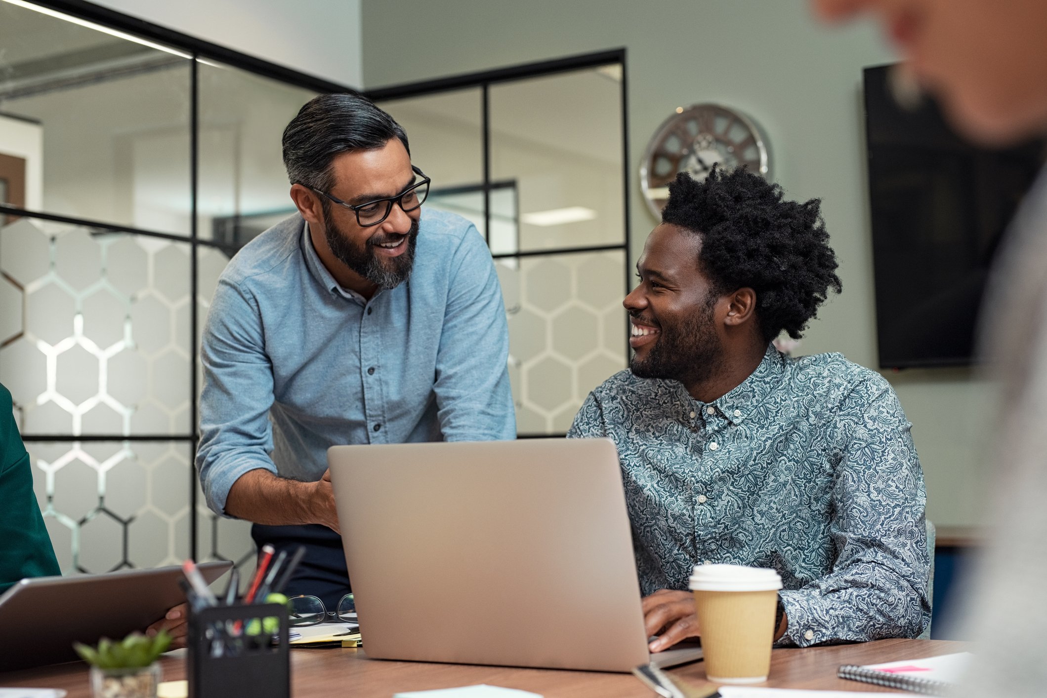 Man at laptop talking to man leaning over his desk