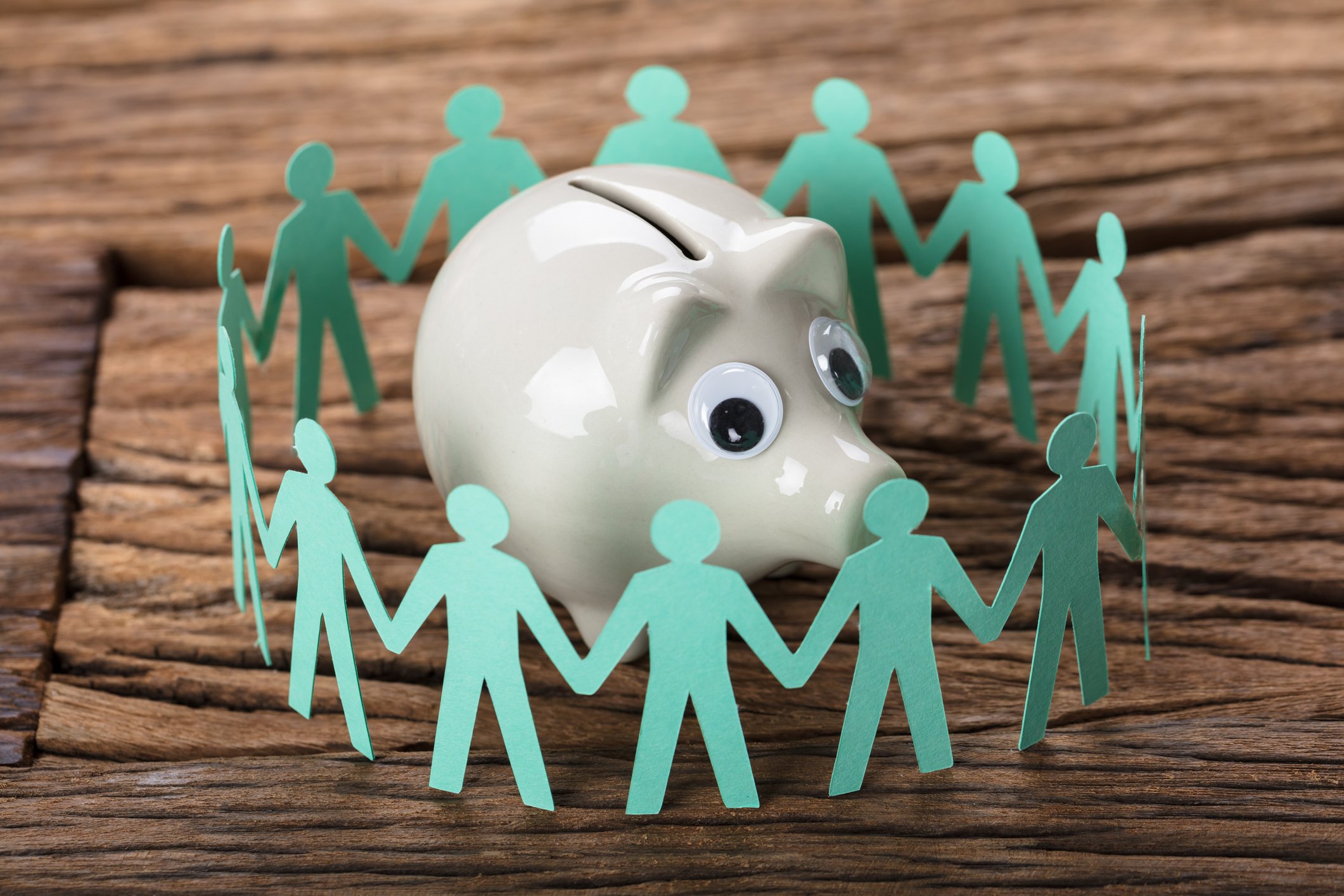 Paper people encircle a piggy bank.