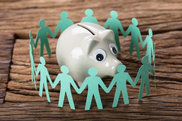 Paper people encircle a piggy bank.