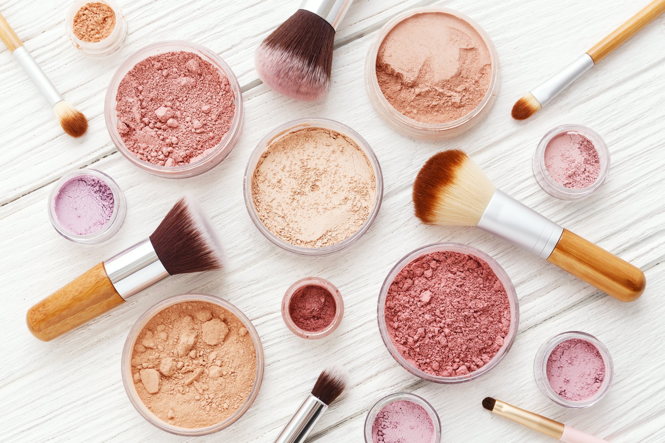 Various pots of makeup powders with makeup brushes scattered around them