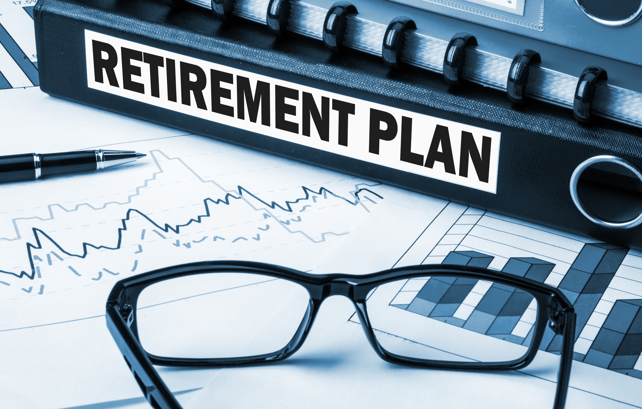 Binder marked Retirement Plan on top of graphs, with a pen and glasses nearby.