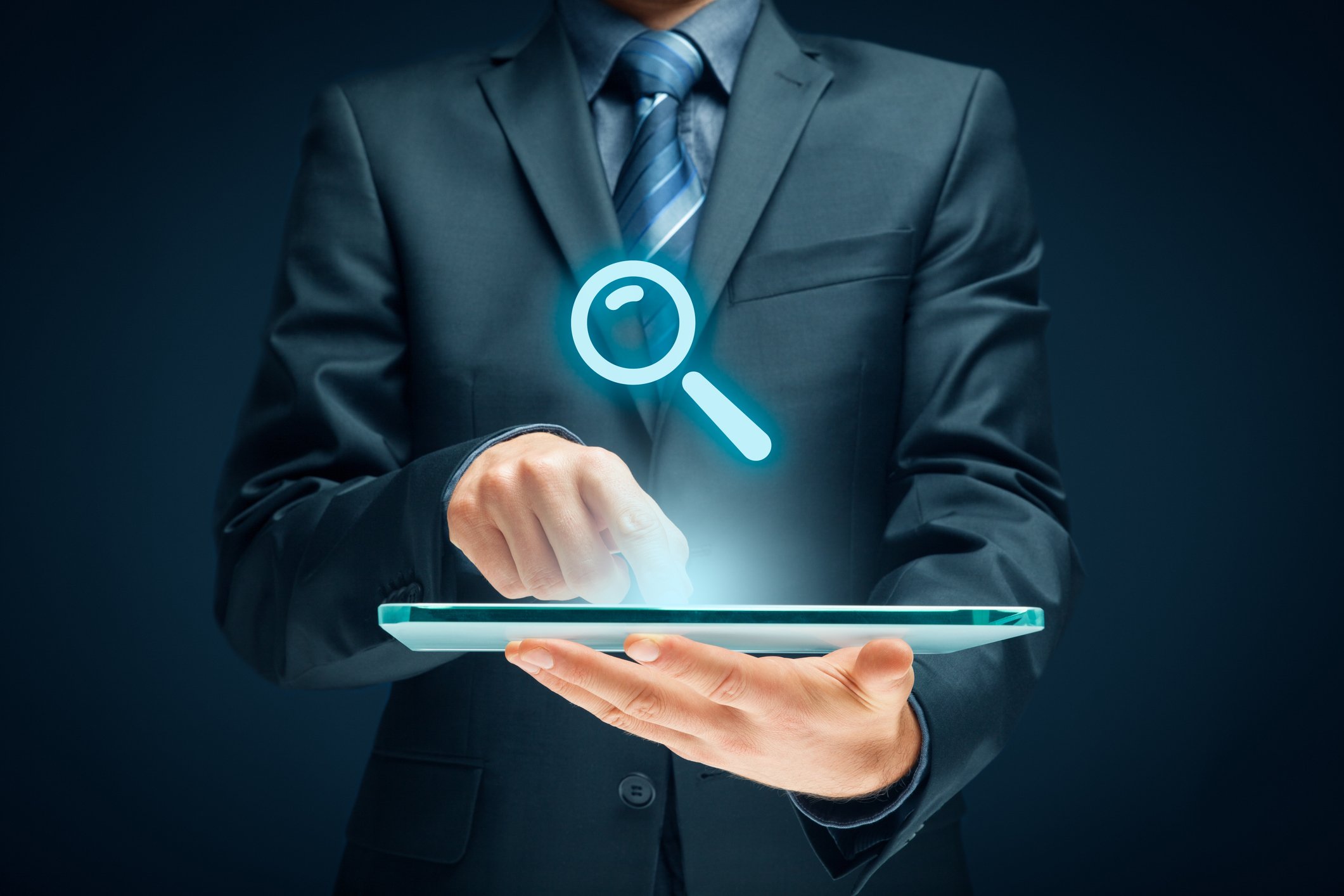 A person pointing to a tablet computer with a holographic image of a magnifying glass above it.