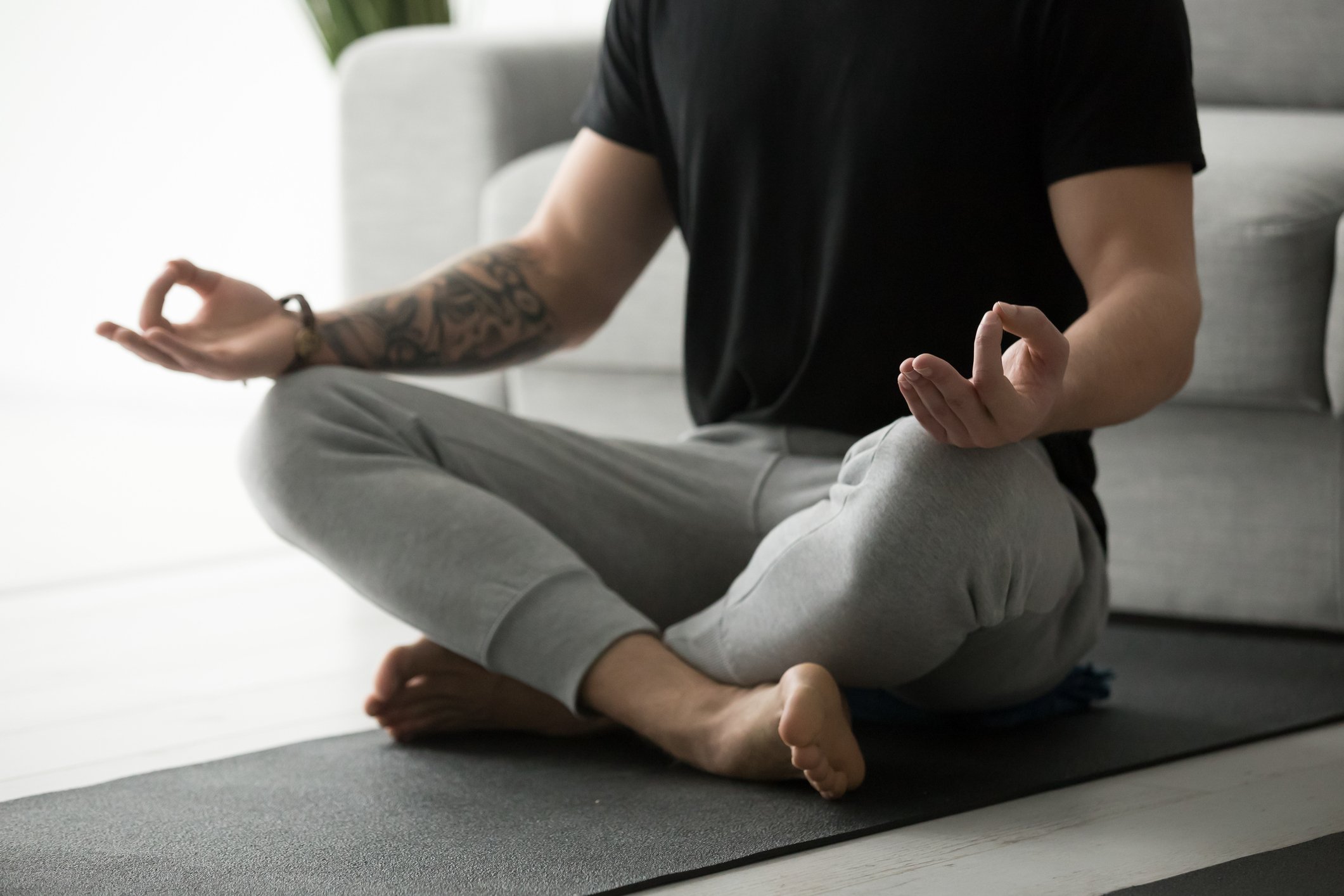 A man sitting in on the floor practicing meditation with his palms facing upward while resting on his knees