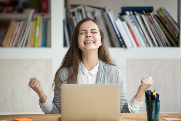 A woman celebrates in front of her laptop.
