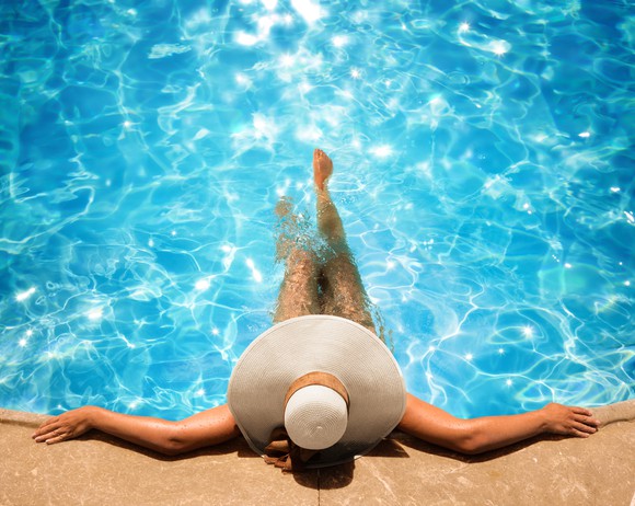 A woman in a sun hat lounges at the edge of a pool