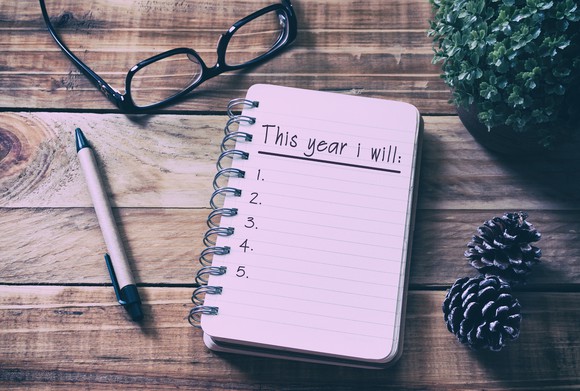 A spiral notebook showing a page headed "This year I will...," with a pen and a pair of eyeglasses