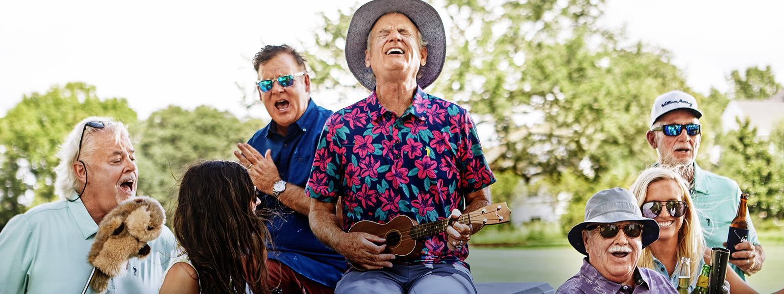 Bill Murray plays a ukelele surrounded by four of his brothers and two women on a golf course. 