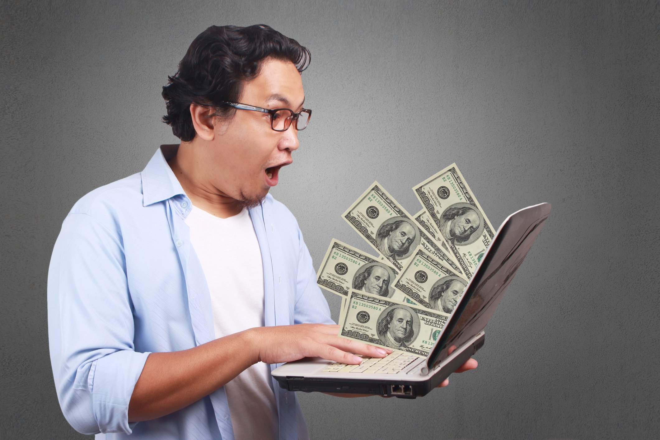 A man reacts with surprise as hundred-dollar bills pop out of his laptop screen.
