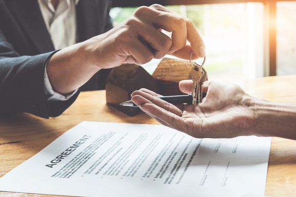 A person hands a set of keys across a desk to a person signing an agreement.
