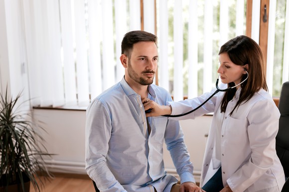 Female doctor with stethoscope on male patient's chest.