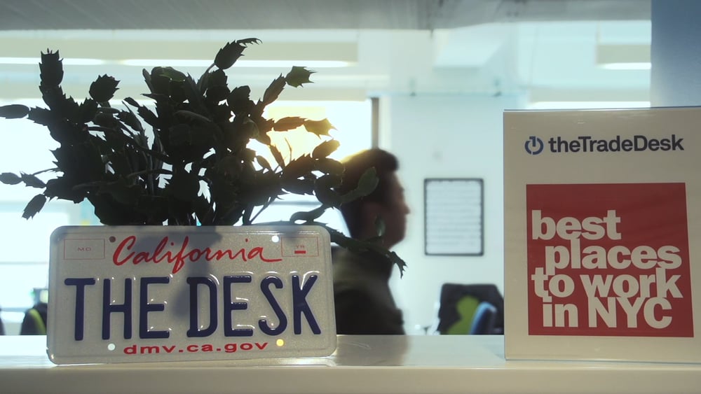 The Trade Desk reception area at its headquarters featuring a potted plant behind a license plate with The Desk California etched on it.
