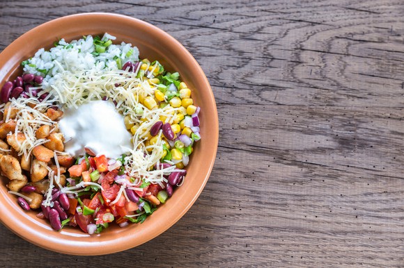 An overhead view of a burrito bowl sitting on a wooden table.