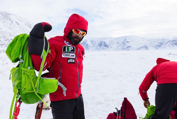 A man in an arctic scene puts on a backpack.