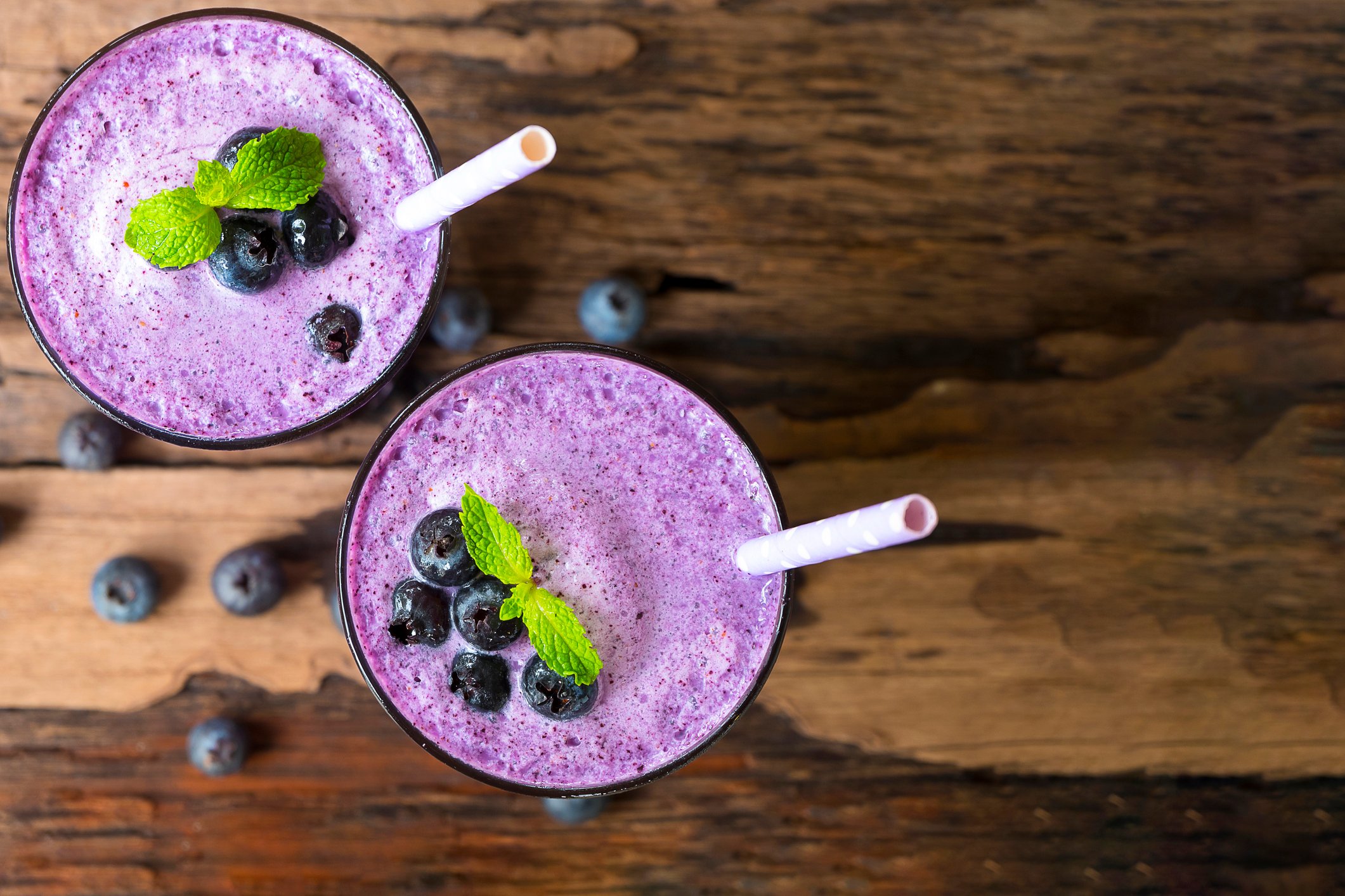 Two blueberry smoothies on a wooden table, seen from above.