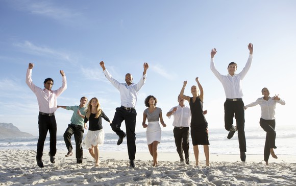 Male and female workers jumping in the air on a beach.